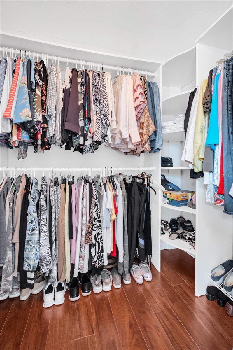 Walk-in closet with double hanging rods, shoe shelves, and reddish-brown flooring.