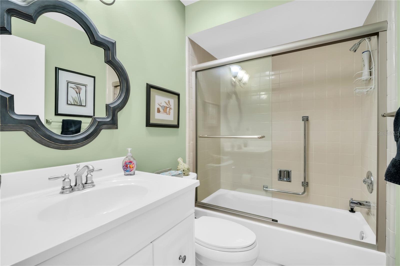 Bathroom with a white vanity and toilet beside a tiled tub-shower with glass doors.