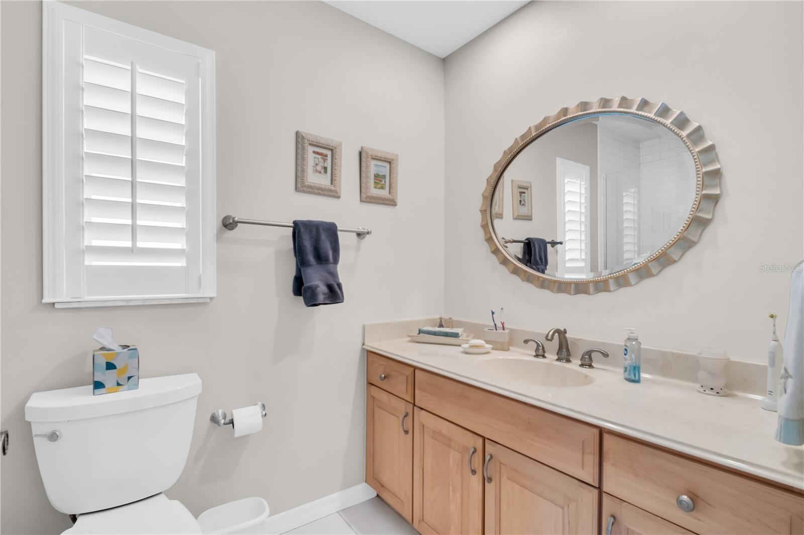 Bathroom with a wood vanity, oval mirror, and plantation shutters.