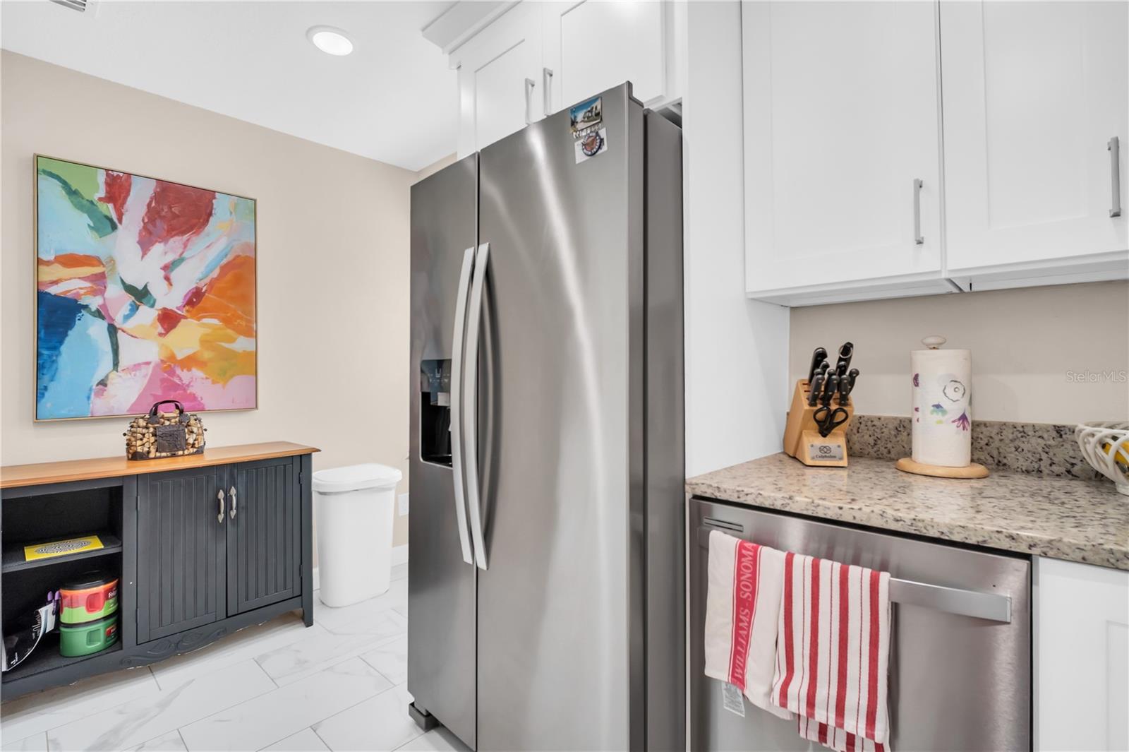 Kitchen with white cabinets, stainless steel appliances, and colorful abstract art above a dark sideboard.
