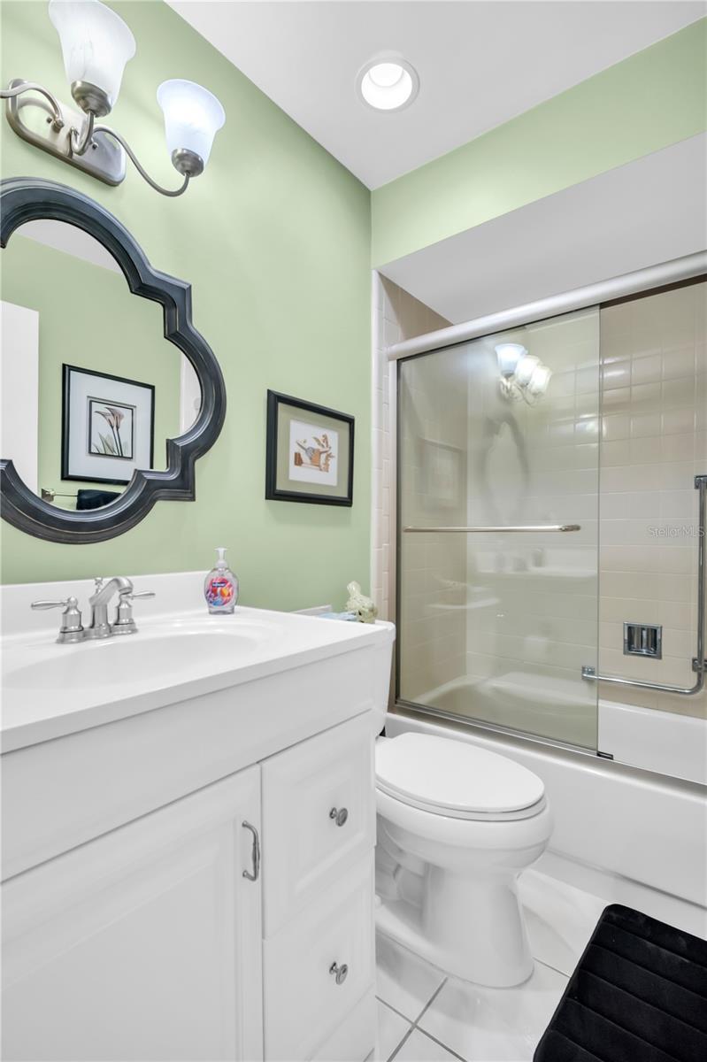 Bathroom with white vanity, ornate mirror, pale green walls, and glass-enclosed tub and shower.