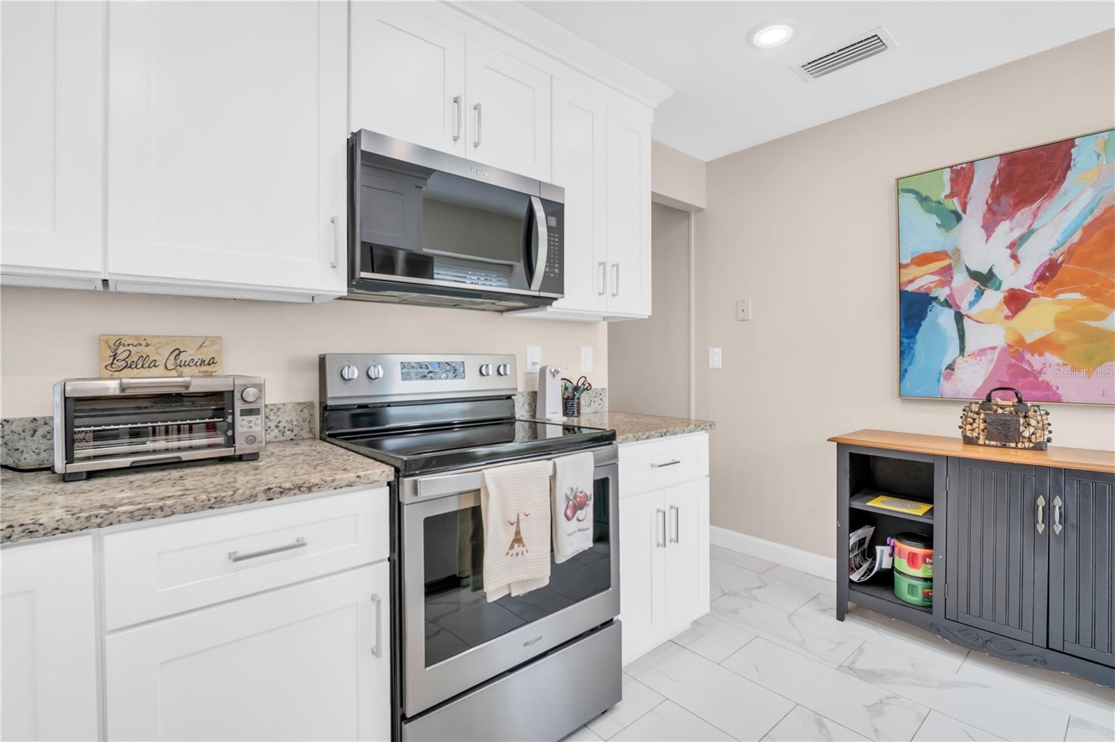 Kitchen with white cabinets, granite counters, stainless-steel appliances, and colorful abstract wall art.