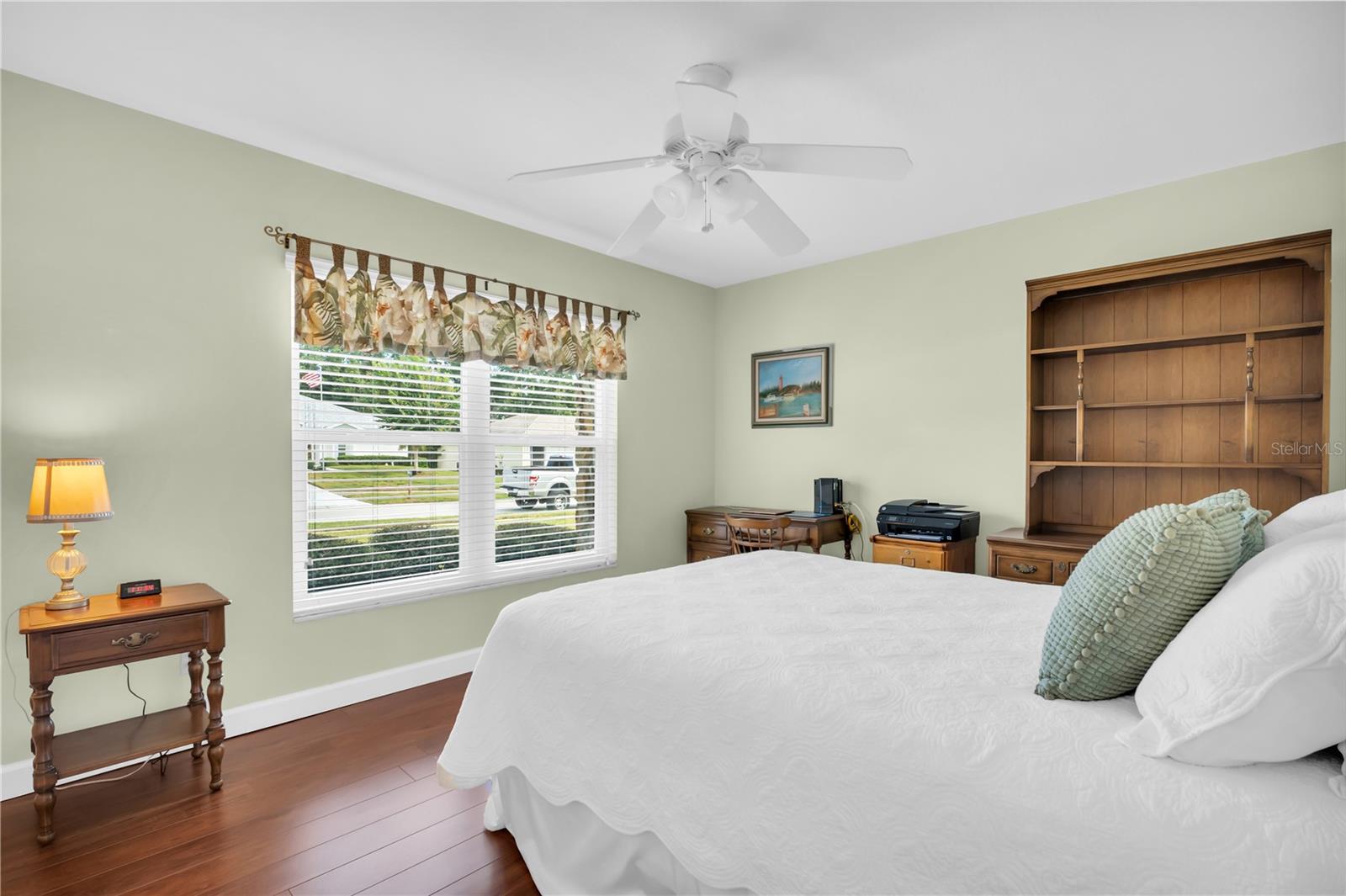 Bedroom with a white bed, wooden built-in shelves, and a large window overlooking the street.