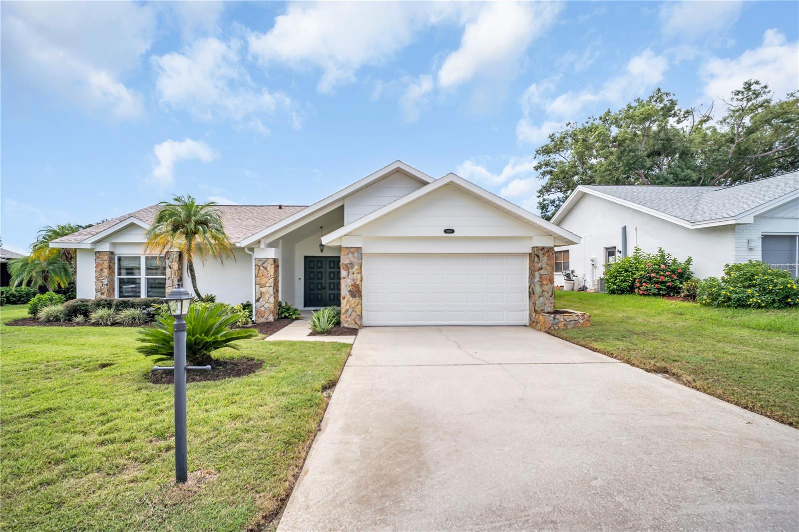 Single-story white house with stone accents, a two-car garage, and palm trees by the driveway.