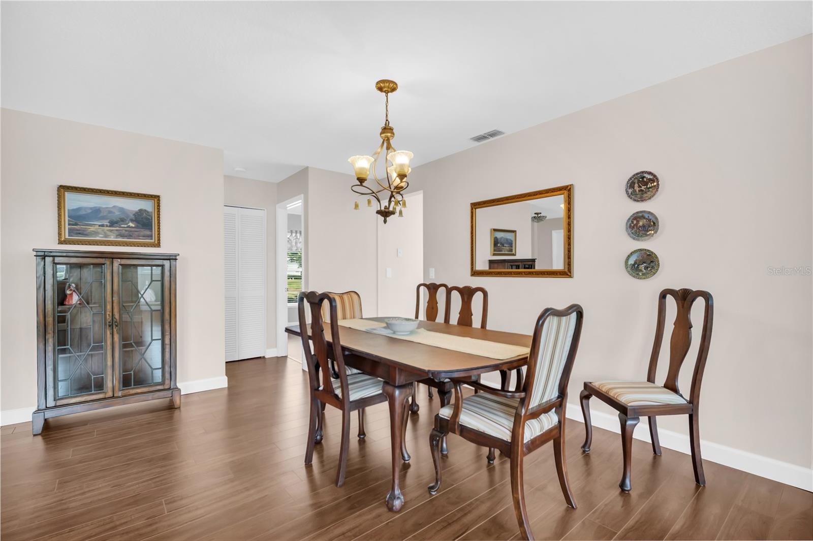 Dining room with a wooden table, upholstered chairs, glass-front cabinet, and brass chandelier.