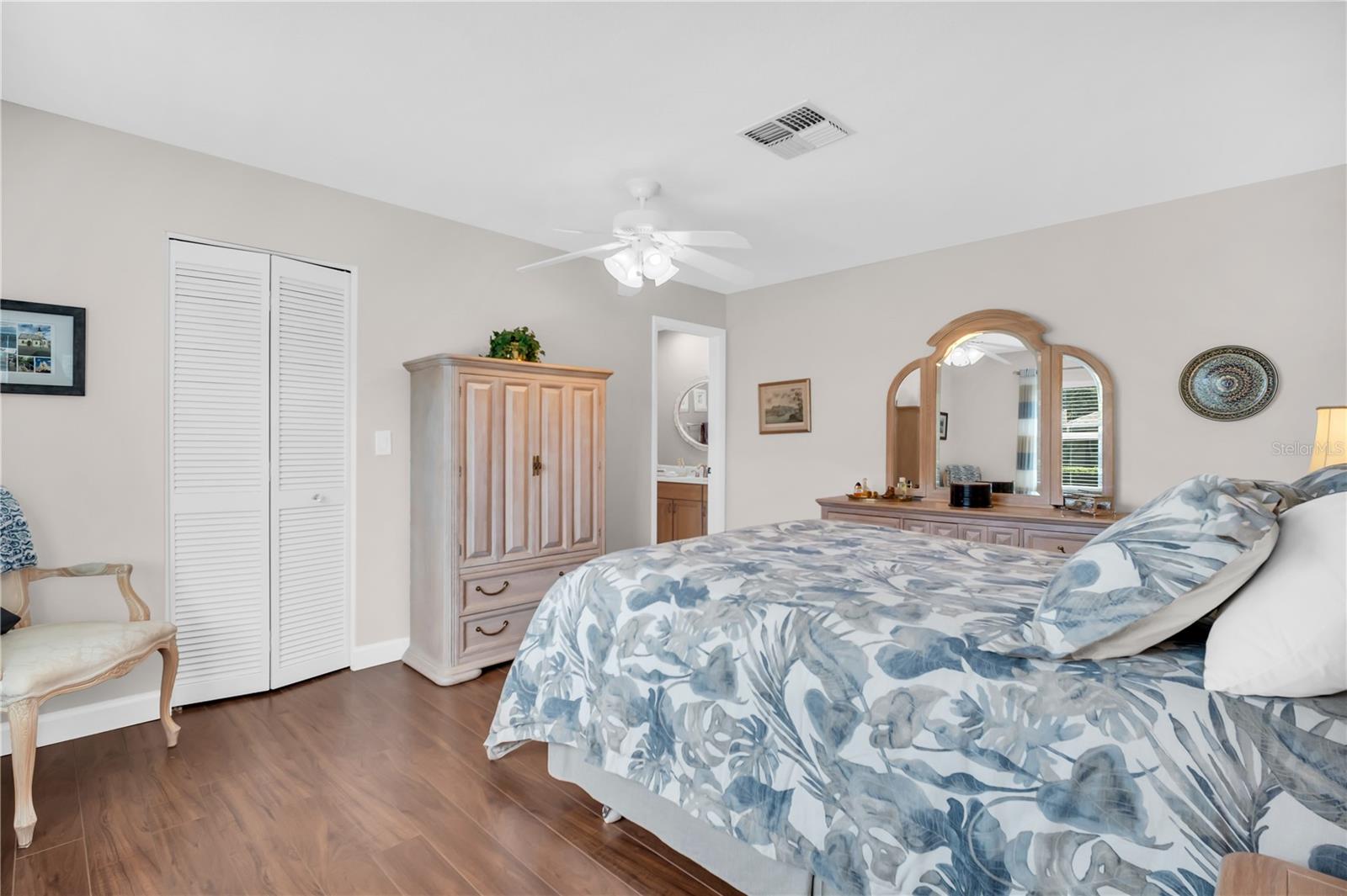 Bedroom with blue floral bedding, a mirrored dresser, louvered closet doors, and a ceiling fan.