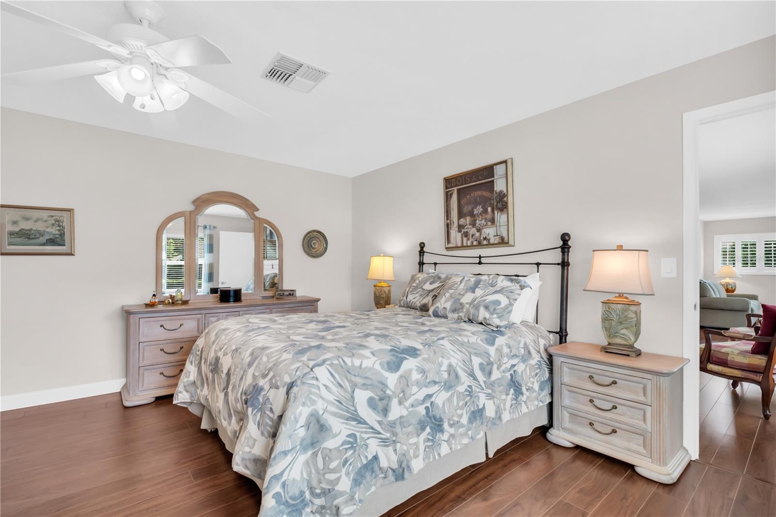 Furnished bedroom with blue-gray floral bedding, matching wood furniture, and an open doorway to the living room.