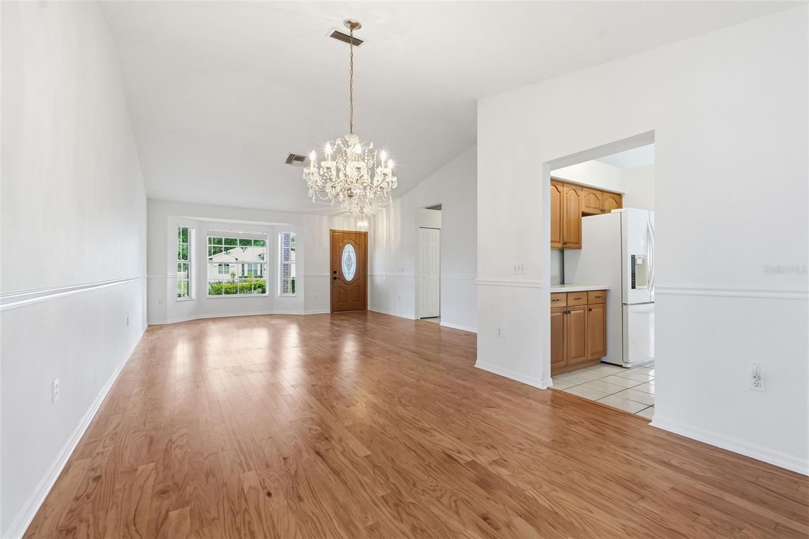 Unfurnished living and dining area with wood floors, a vaulted ceiling, and a crystal chandelier.