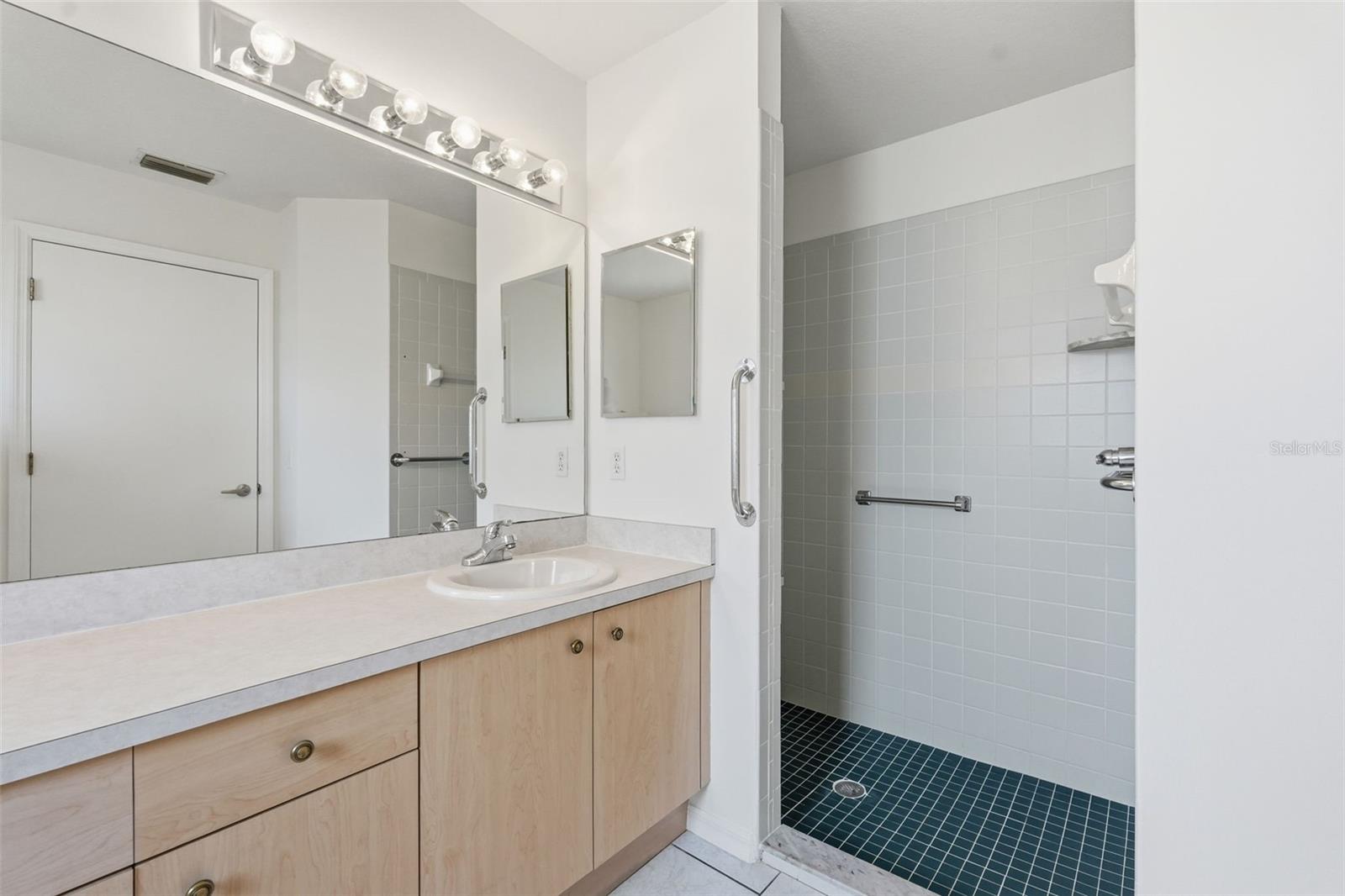 Bathroom with a light wood vanity and tiled walk-in shower with grab bars.
