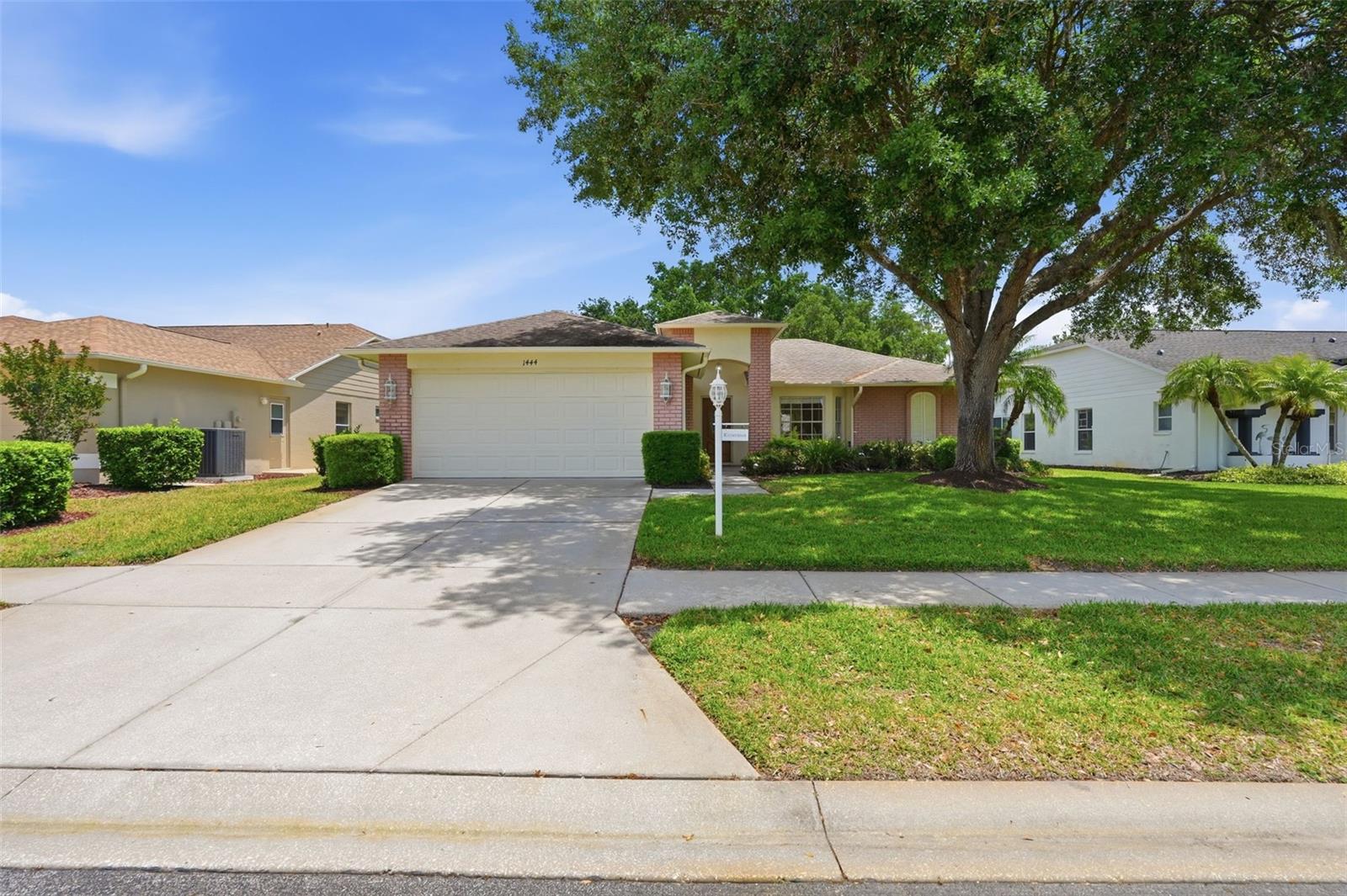 Single-story home with brick accents, a two-car garage, and a large shade tree over the lawn.