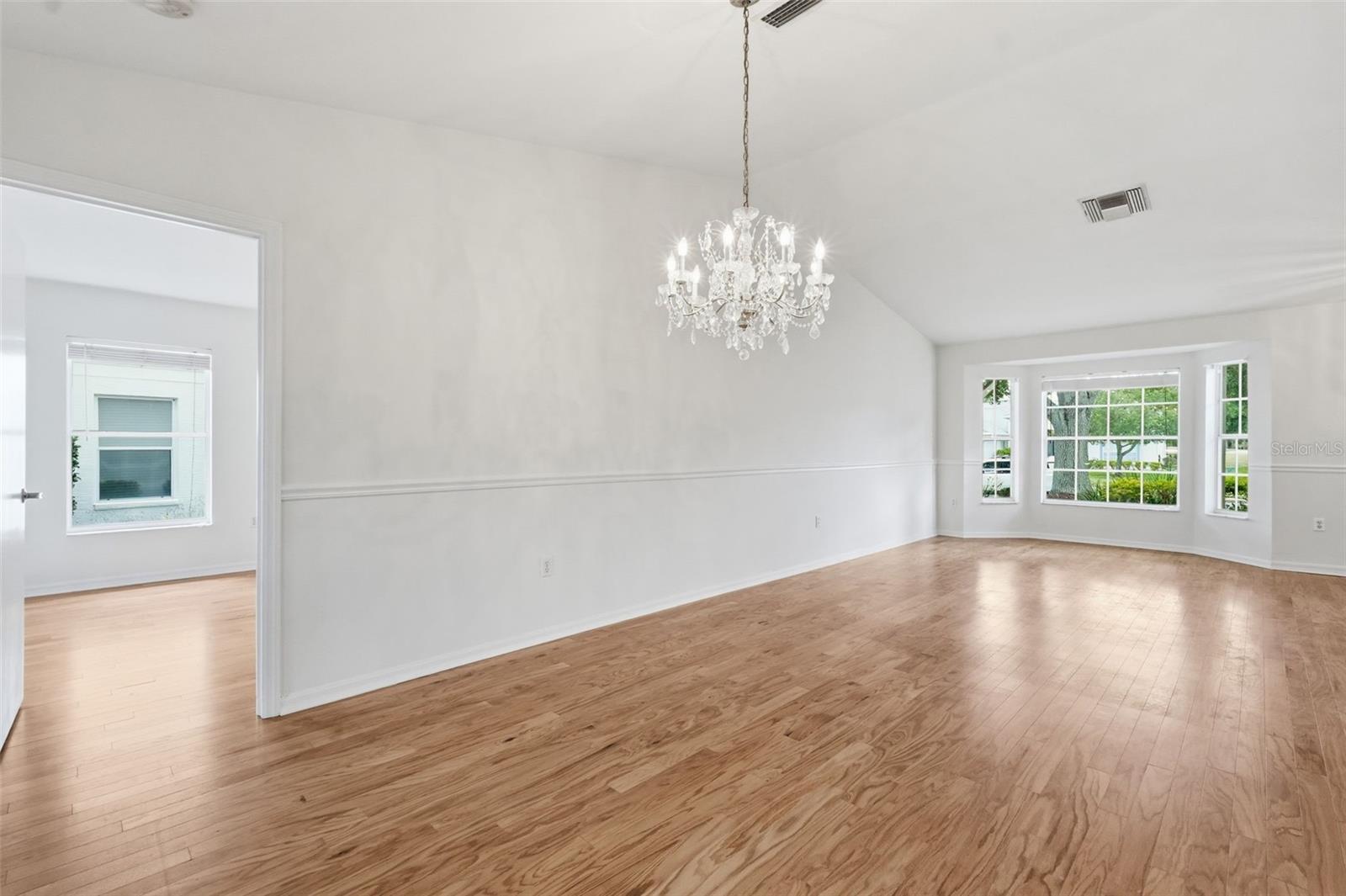 Empty dining room with hardwood floors, crystal chandelier, and large windows.