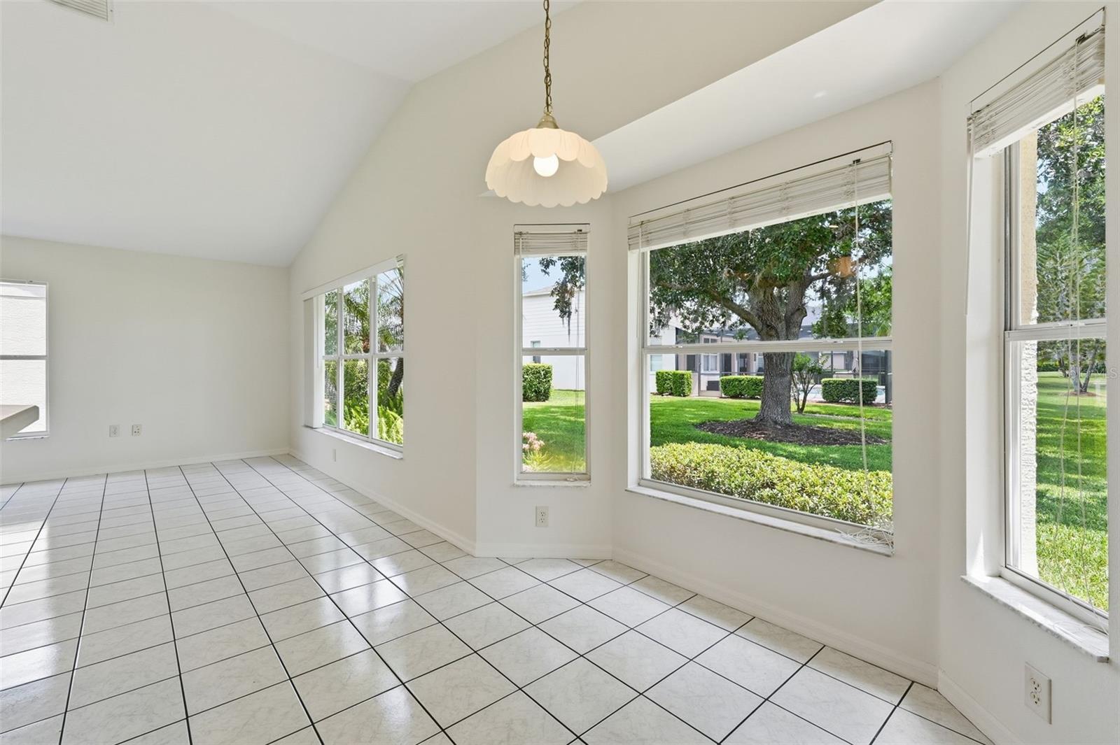 Empty tiled room with a vaulted ceiling and large windows overlooking a green yard.
