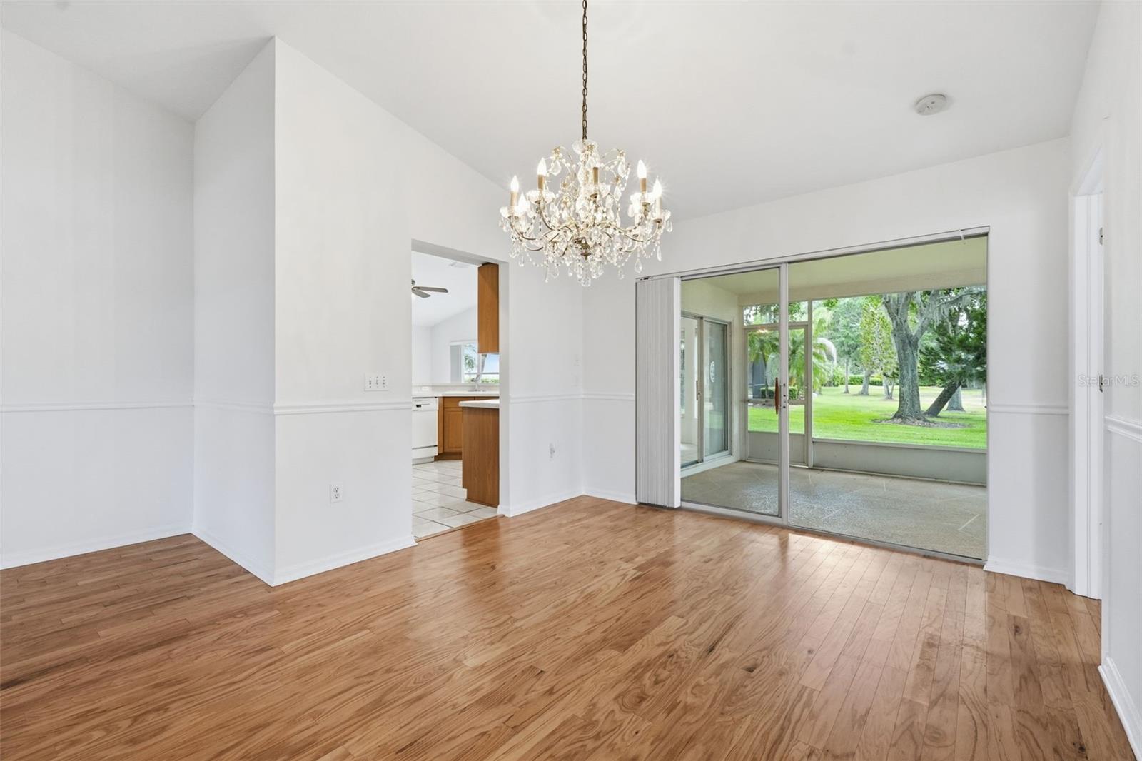 Empty living and dining area with hardwood floors, crystal chandelier, and sliding doors to a screened patio.