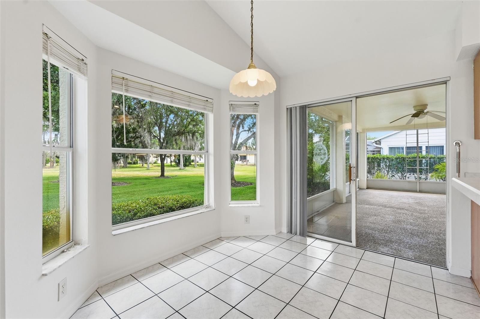 Tiled sunroom with large windows overlooking a lawn and sliding doors to a covered patio.