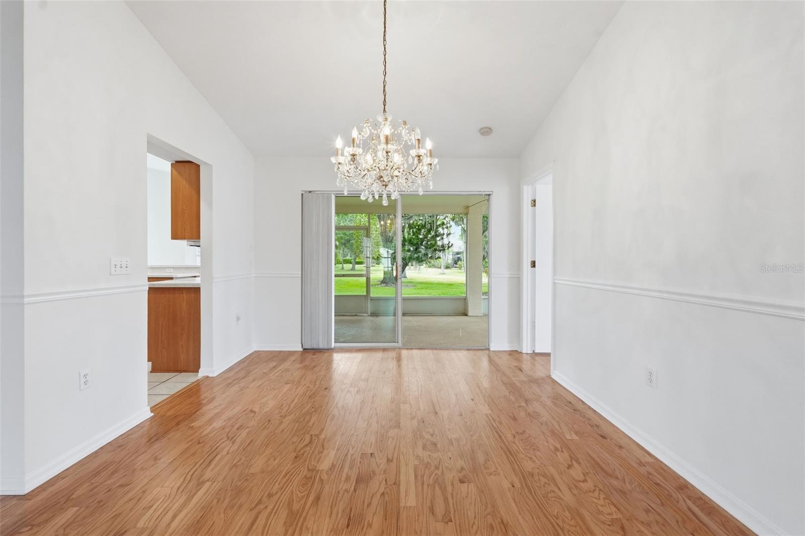 Empty dining room with hardwood floors, a crystal chandelier, and sliding doors to a glass-enclosed patio.