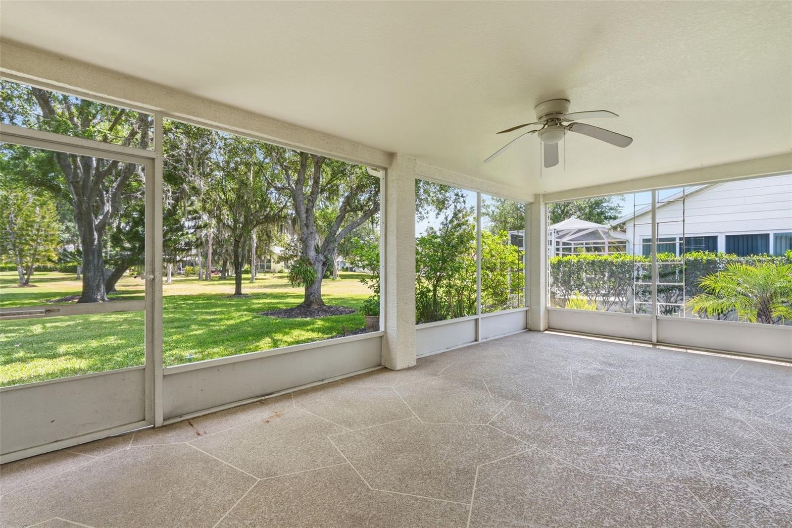 Screened patio with a tiled floor and ceiling fan overlooking mature trees.