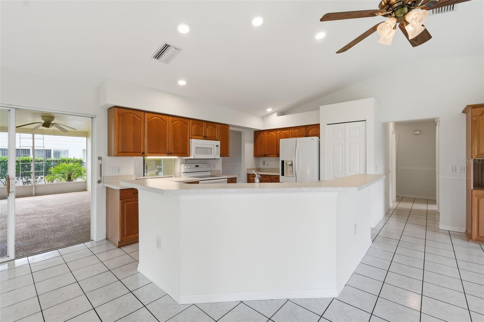 Kitchen with a large white peninsula, wood cabinets, and sliding doors to an adjoining carpeted room.