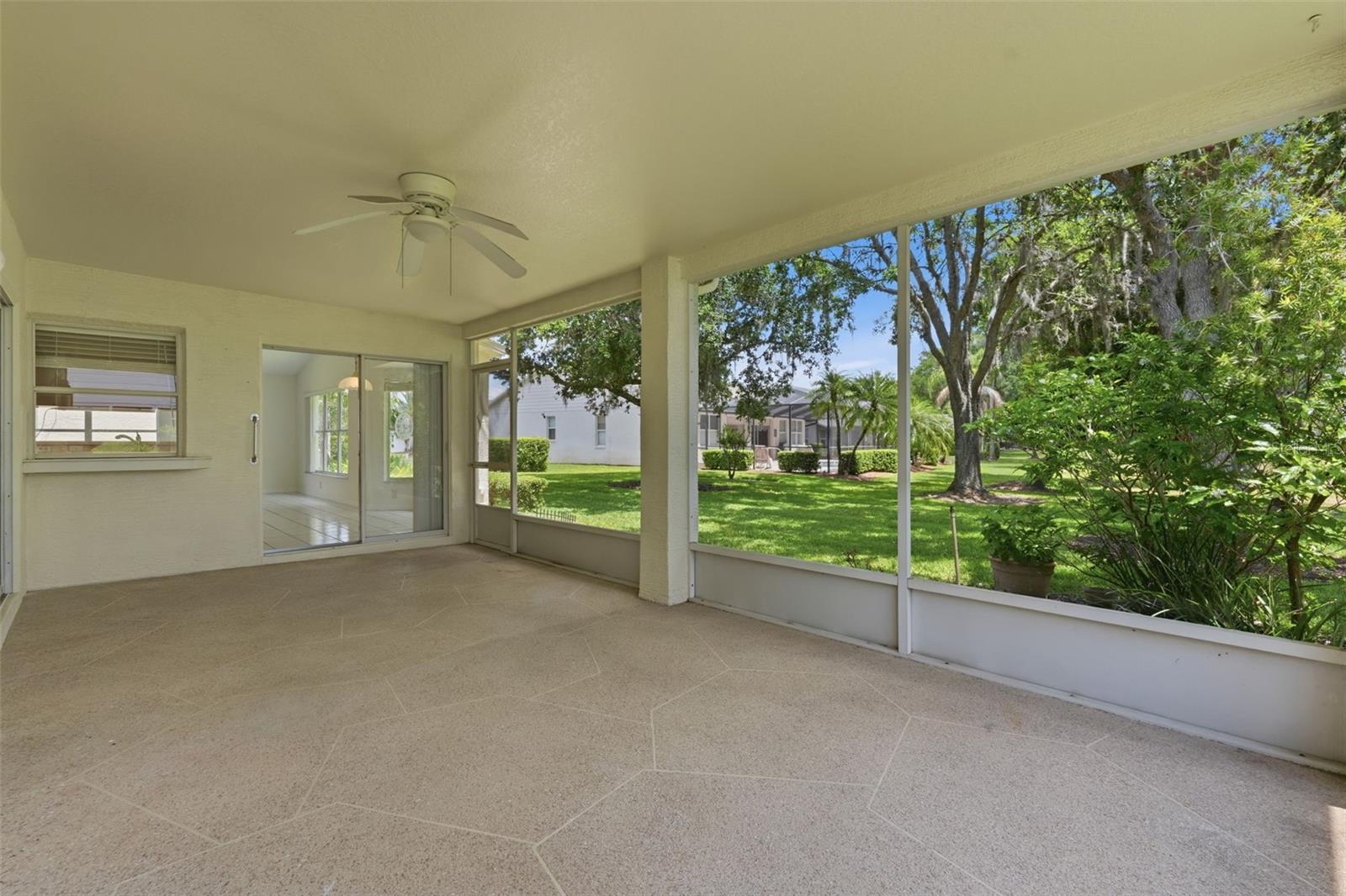 Screened patio with a tiled floor and ceiling fan overlooking a leafy backyard.
