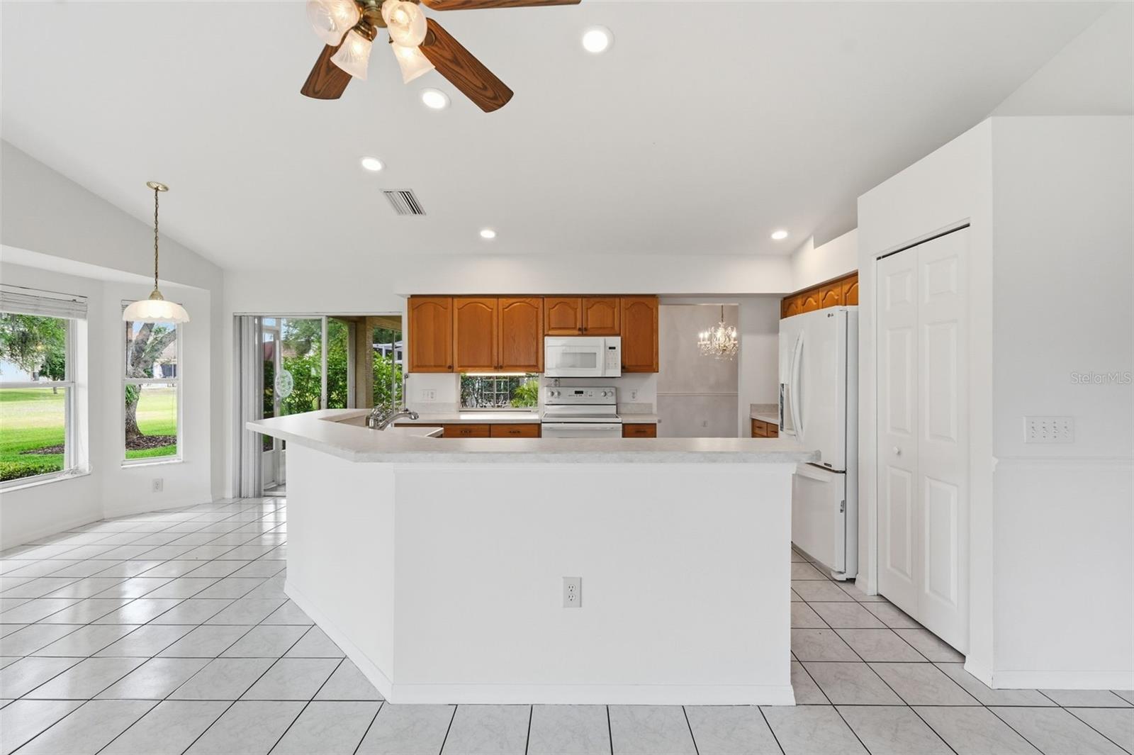 Open kitchen with a large white peninsula, warm wood cabinets, and windows overlooking the lawn.