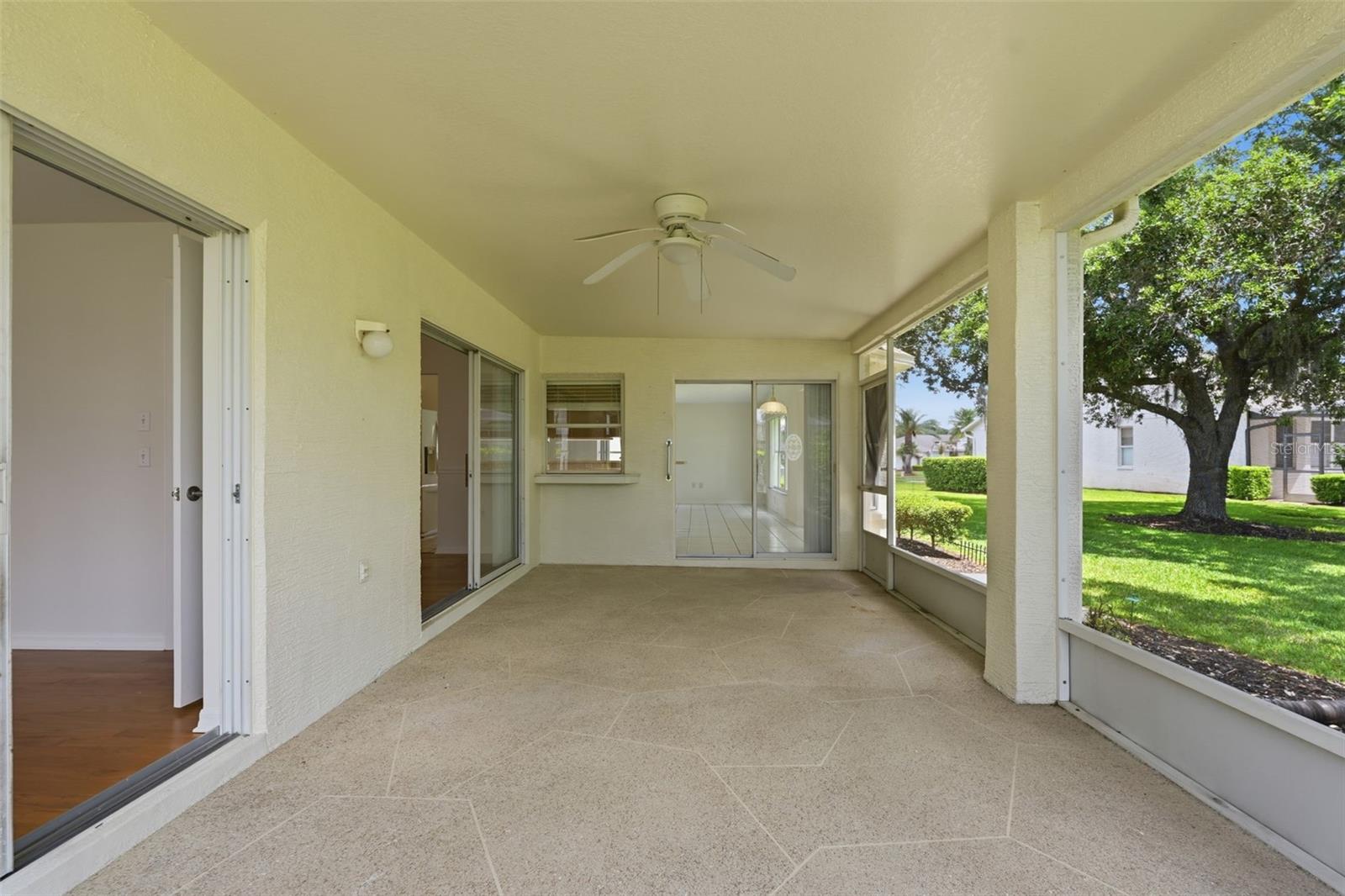 Covered screened patio with tiled floor and ceiling fan overlooking a lawn and shade tree.