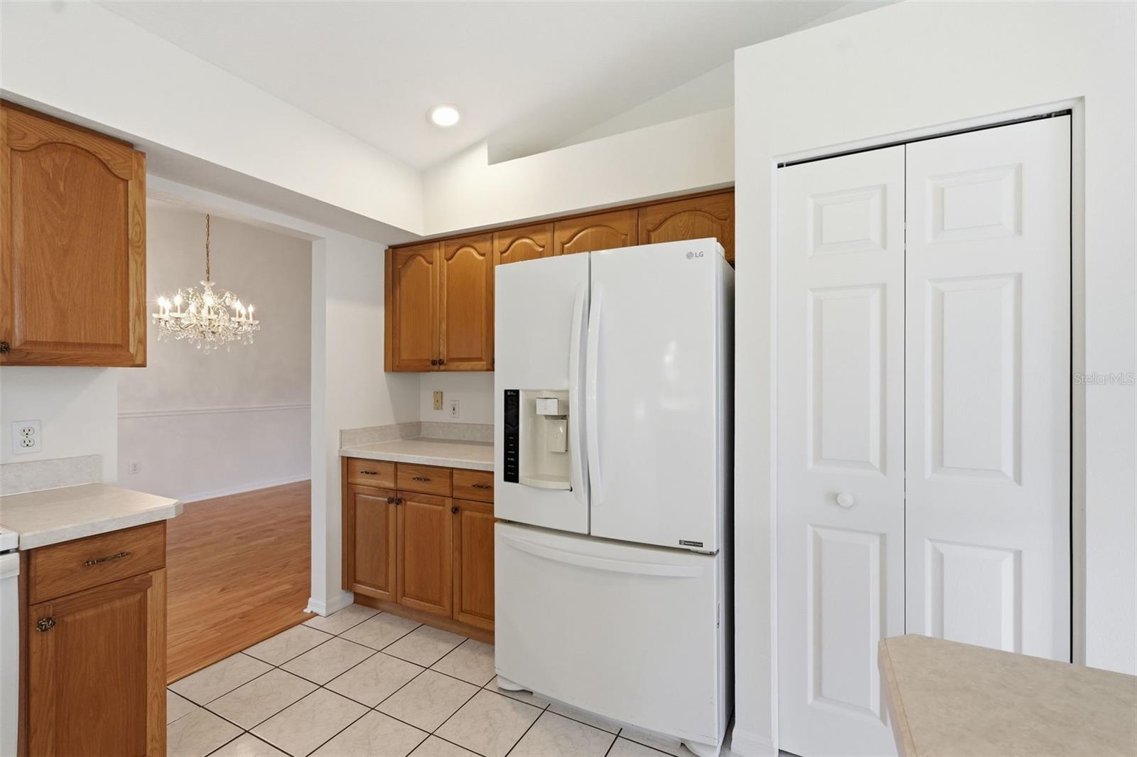 Kitchen with wood cabinets, a white refrigerator, tiled floor, and an adjoining dining area with chandelier.