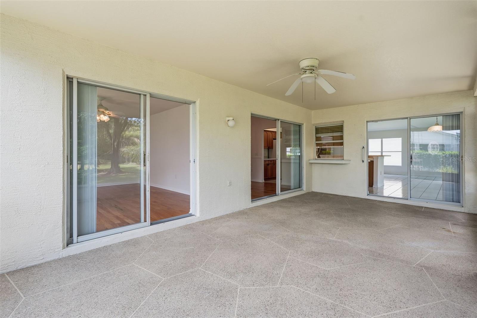 Covered patio with large tile flooring, ceiling fan, and sliding glass doors.