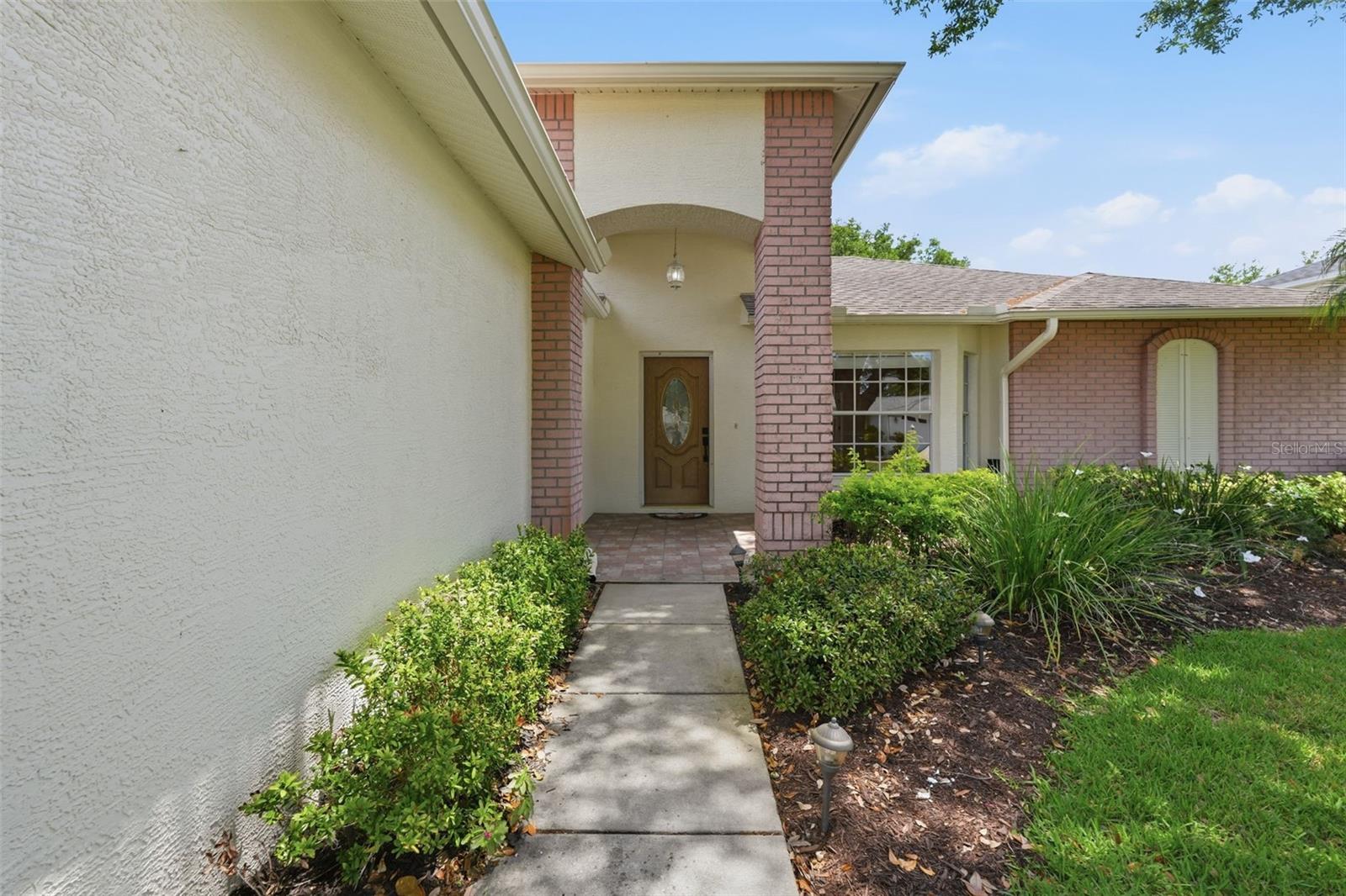 Home's covered front entrance with brick columns, a decorative wooden door, and a landscaped walkway.