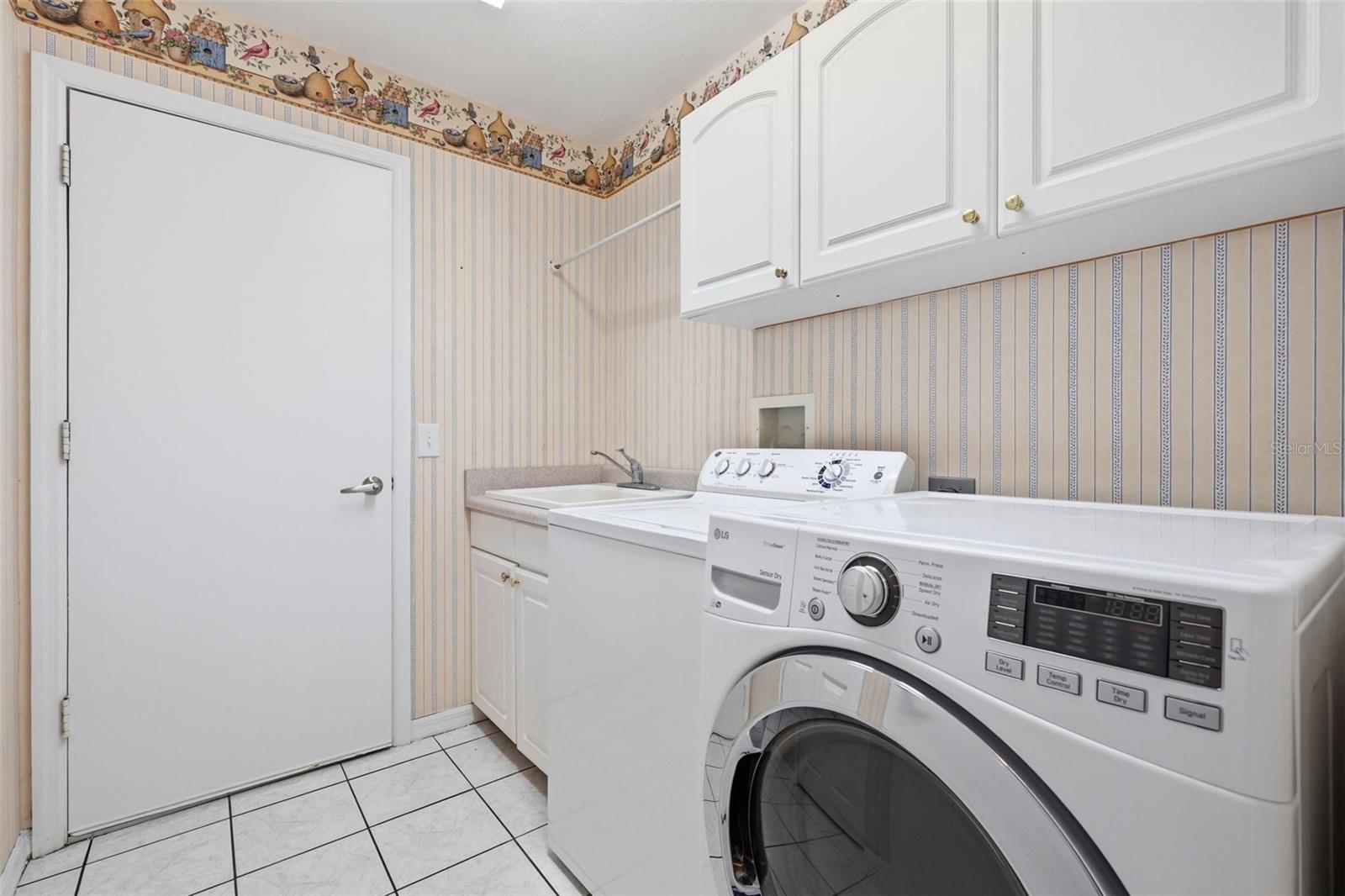 Laundry room with front-loading washer and dryer, utility sink, and overhead cabinets.