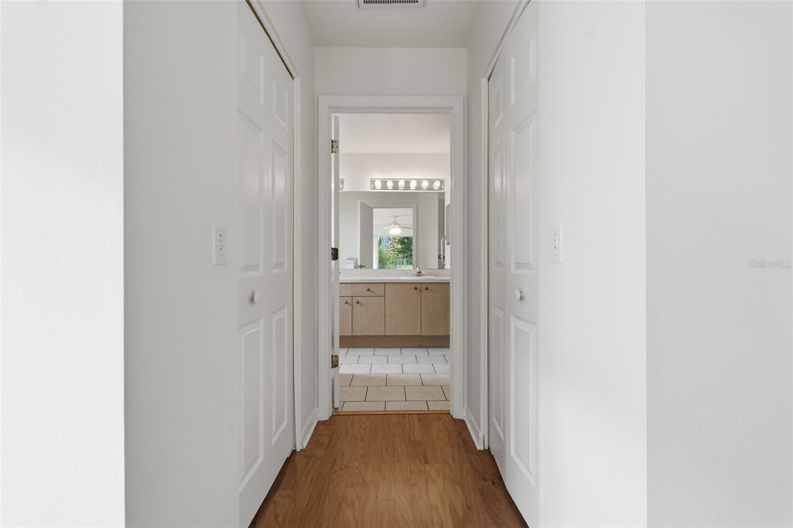 Hallway with hardwood floors and white paneled doors leading to a bathroom with a light wood vanity.