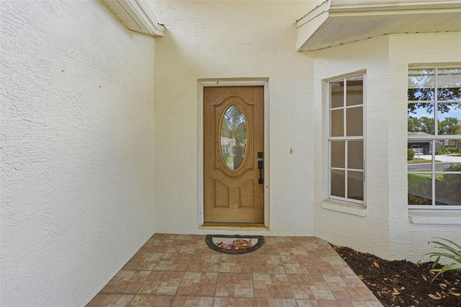 Home’s covered entry with a wood oval-glass front door and tiled porch.