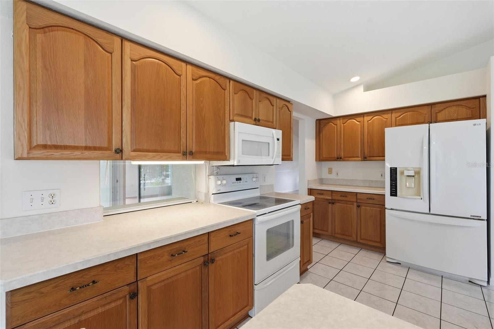 Kitchen with honey-toned wood cabinets, white appliances, and light countertops.