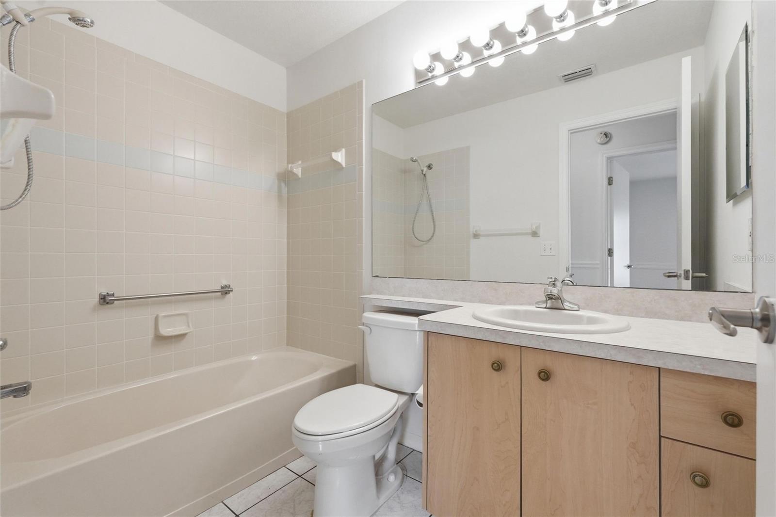 Bathroom with a bathtub, tiled shower wall, toilet, and wood vanity with oval sink.
