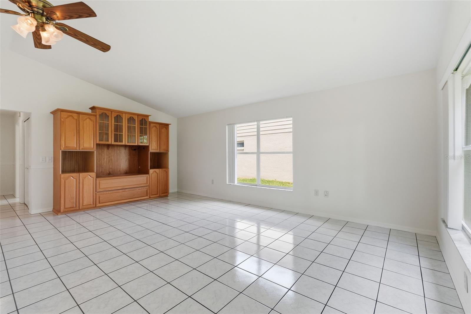 Vacant living room with white tile floors and built-in wooden entertainment cabinetry.