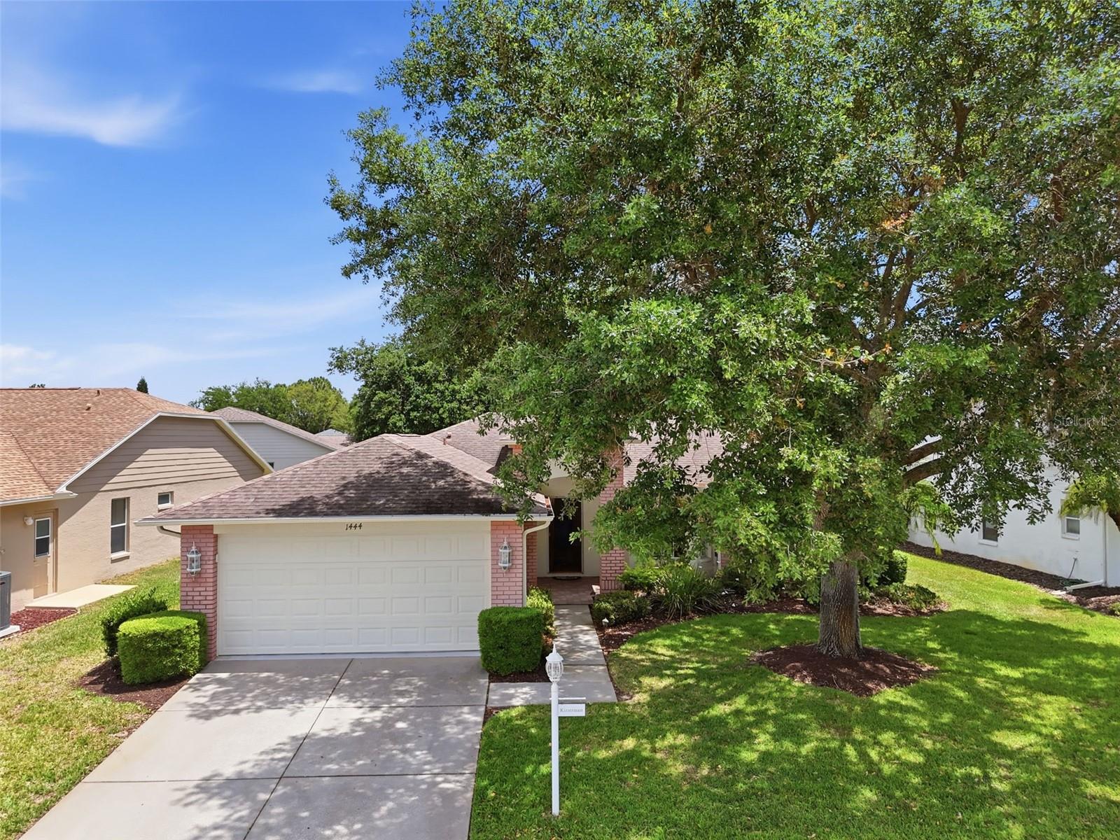 Home with a two-car garage and brick accents, partly shaded by a large front-yard tree.