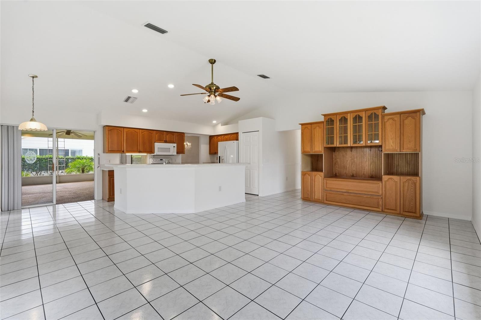 Open kitchen with a white breakfast bar, wood cabinetry, tile floors, and sliding doors to a screened lanai.