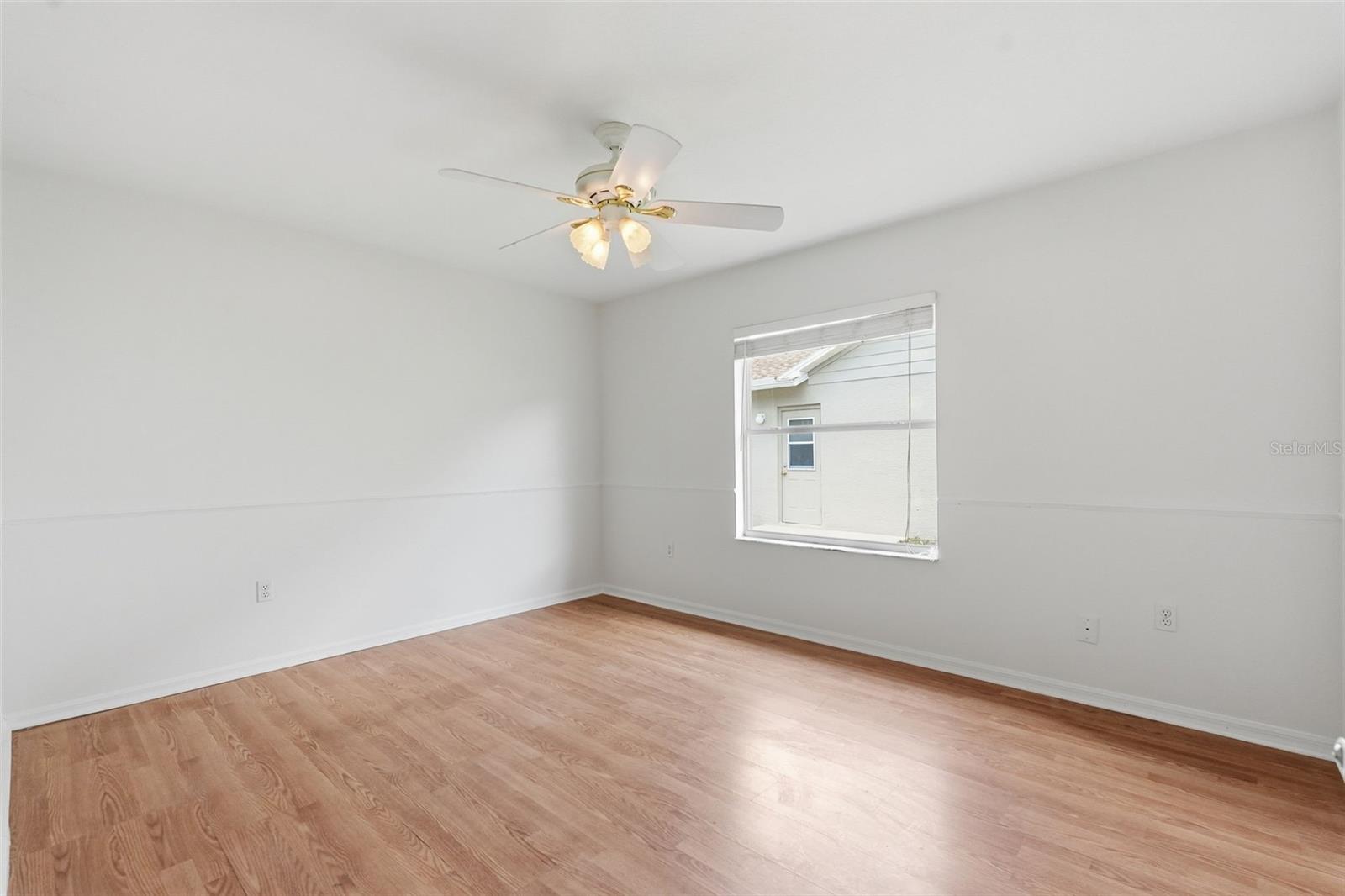 Empty bedroom with wood-look flooring, a ceiling fan, and a window with blinds.