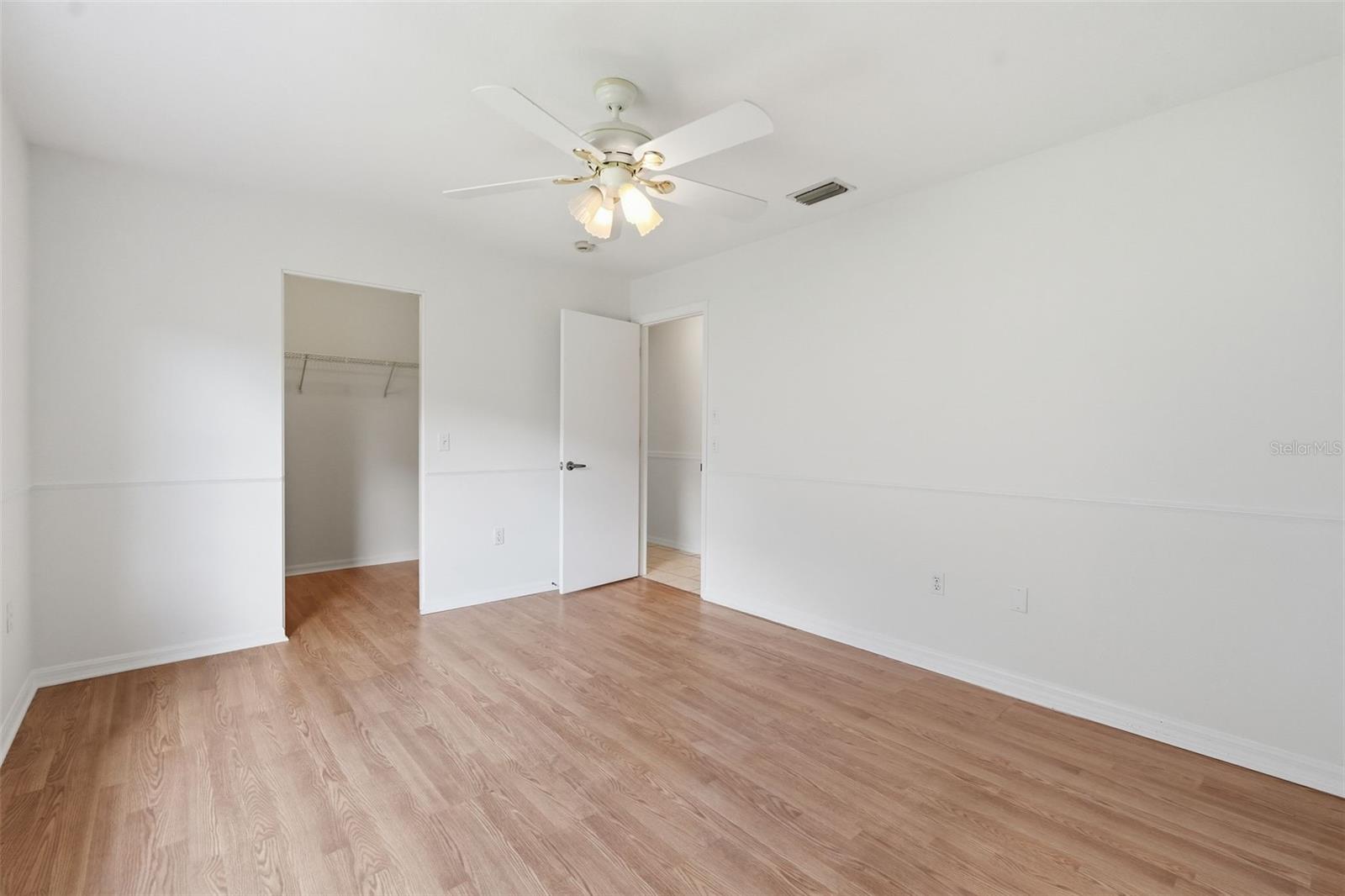 Vacant bedroom with light wood floors, a ceiling fan, and an open closet.