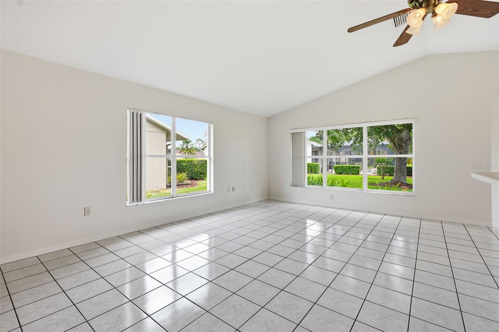 Empty tiled room with two windows overlooking a green yard and a ceiling fan.