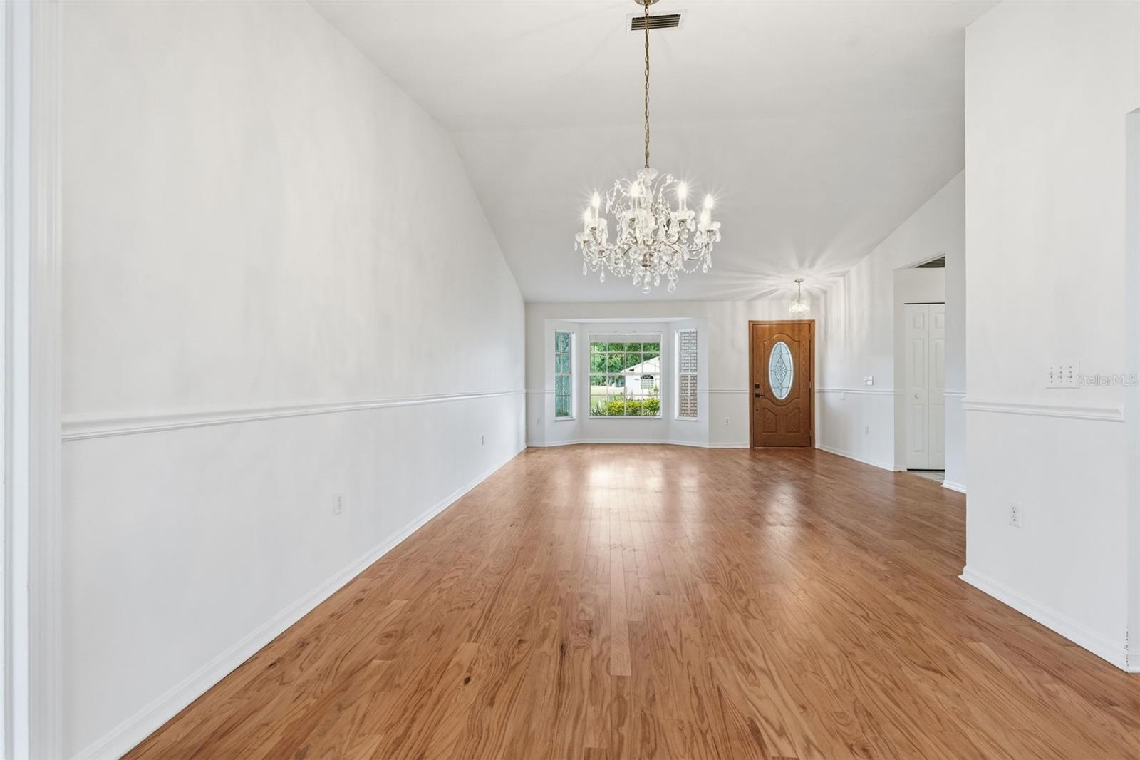 Empty dining room with hardwood floors, a crystal chandelier, and a wooden front door.