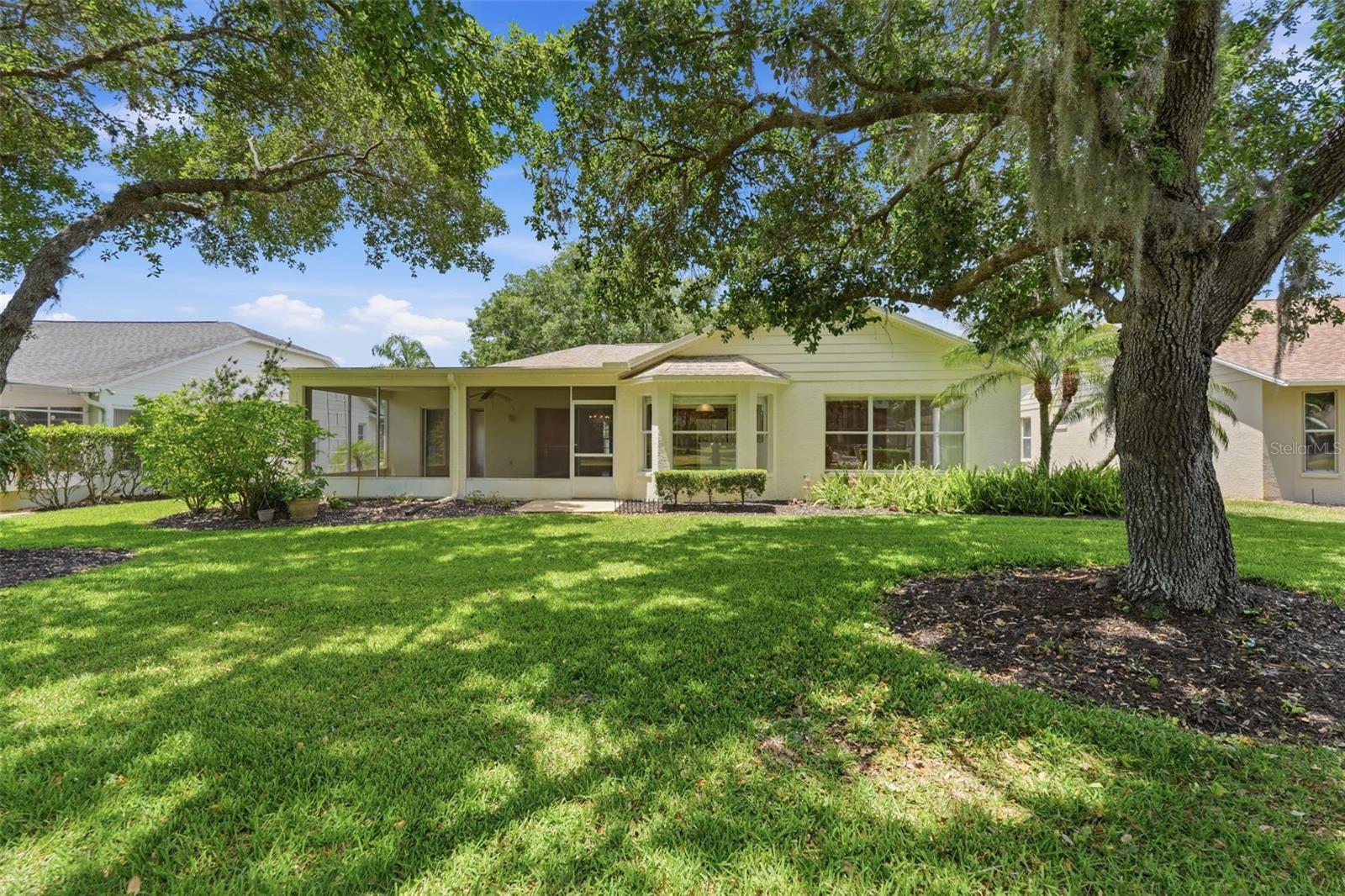 Single-story home with a screened lanai beneath a large oak tree.