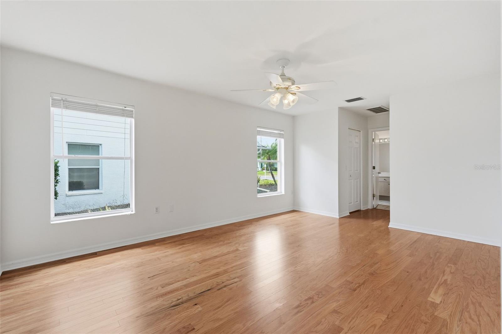 Vacant room with hardwood floors, two windows, and a ceiling fan with lights.