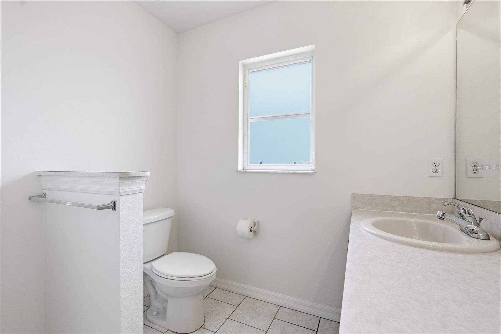Bathroom with a stone vanity, white toilet, tiled floor, and small window.