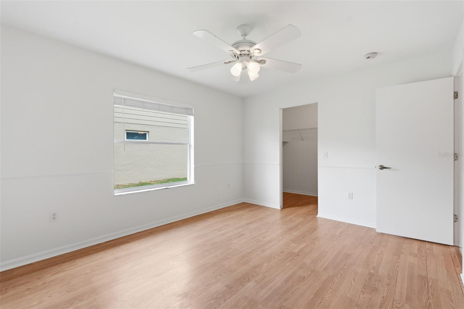 Vacant bedroom with light wood-look floors, a ceiling fan, and a window with blinds.