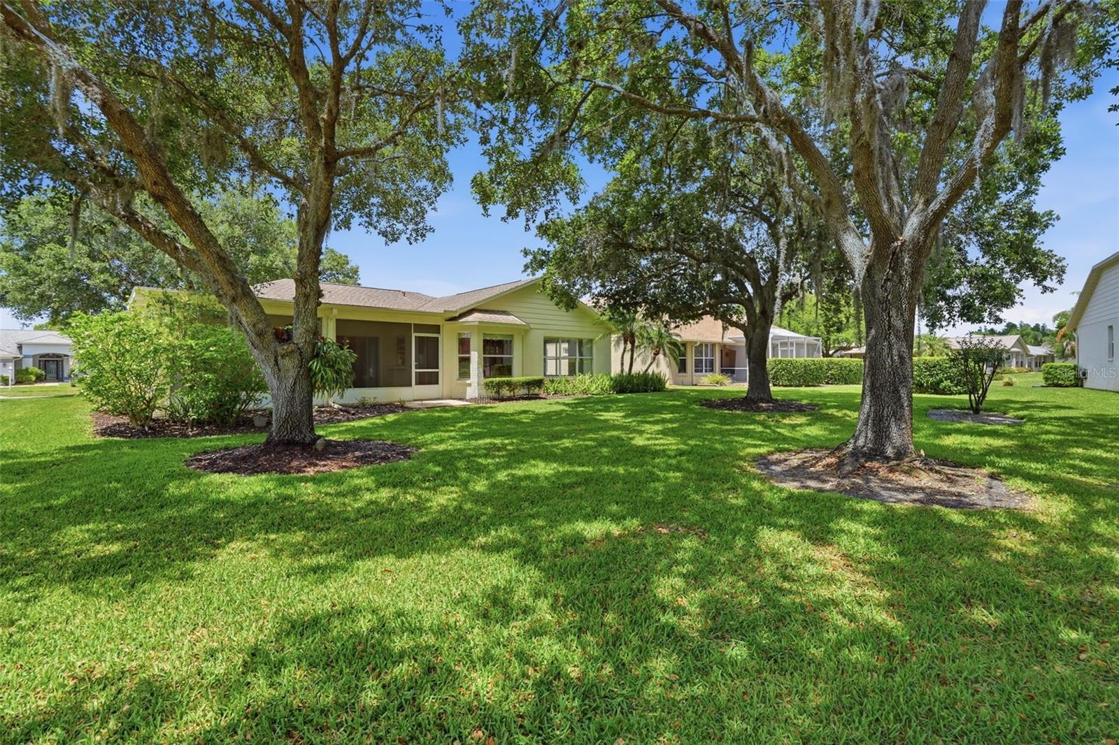 Single-story pale green house with a screened lanai, broad lawn, and mature shade trees.