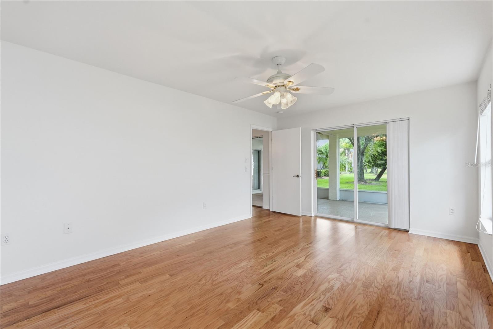 Empty room with hardwood floors and sliding glass doors opening onto a covered patio.