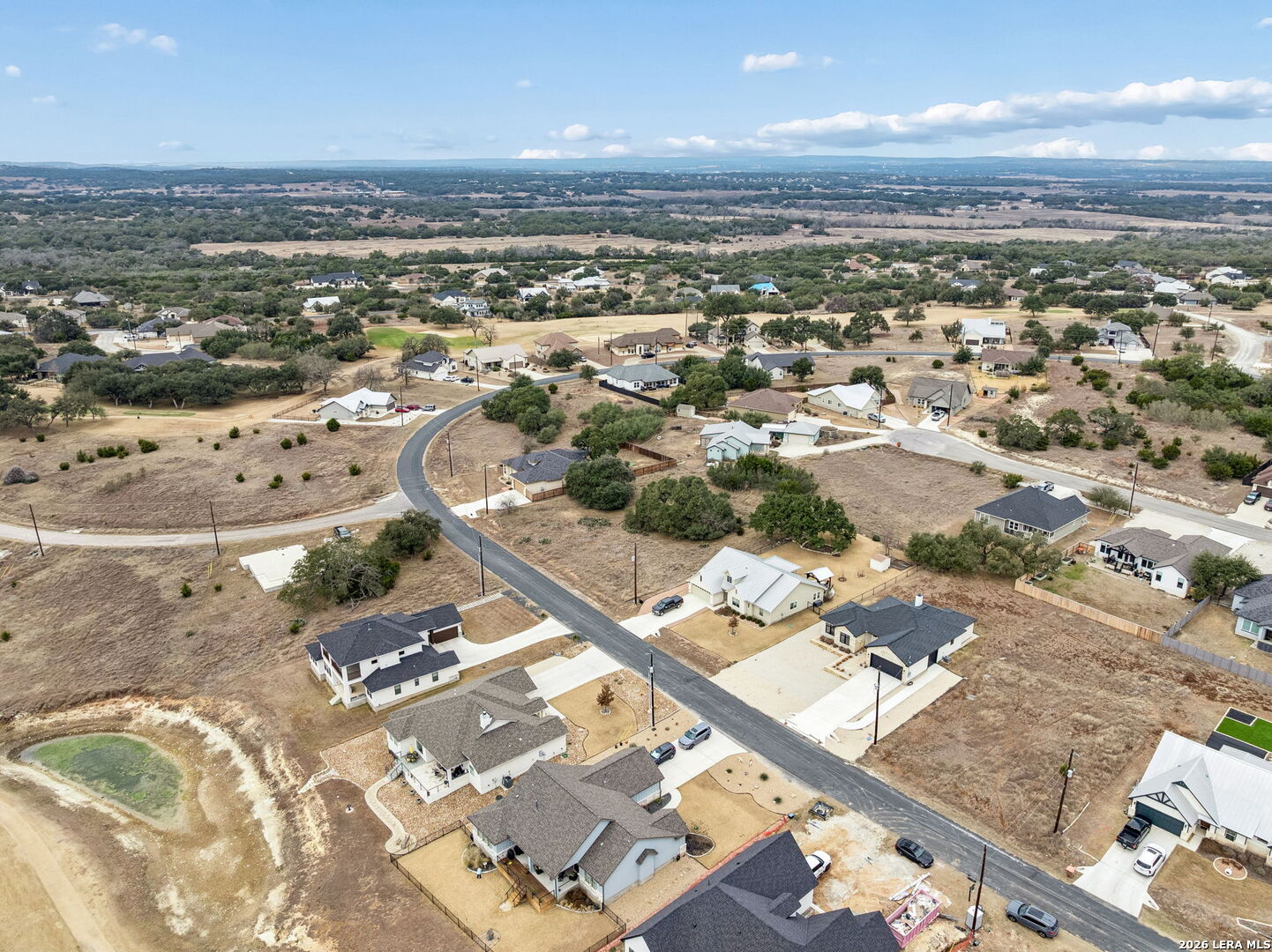 Aerial view of homes and open lots along a curving road in a rural neighborhood.