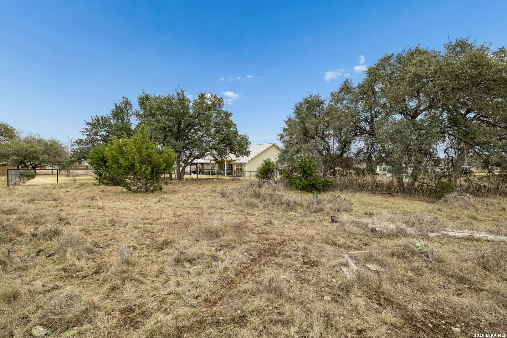 Single-story home beyond a dry, open yard framed by mature oak trees.