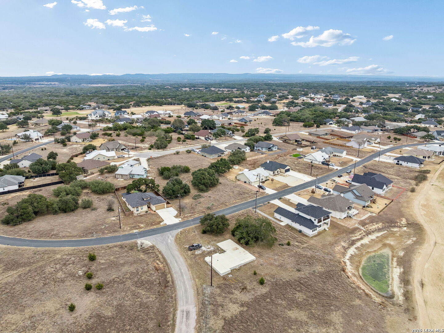 Aerial view of a residential neighborhood with dry open lots and wooded hills in the distance.