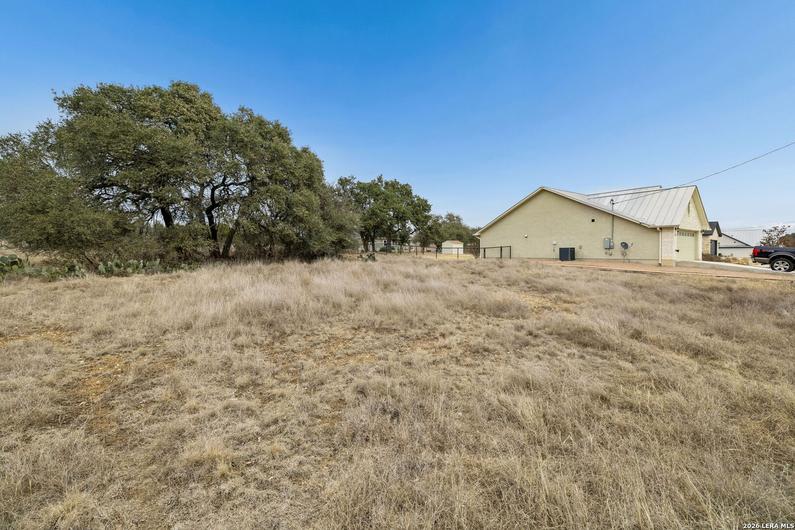 Beige single-story house beside a dry grassy yard with mature oak trees.