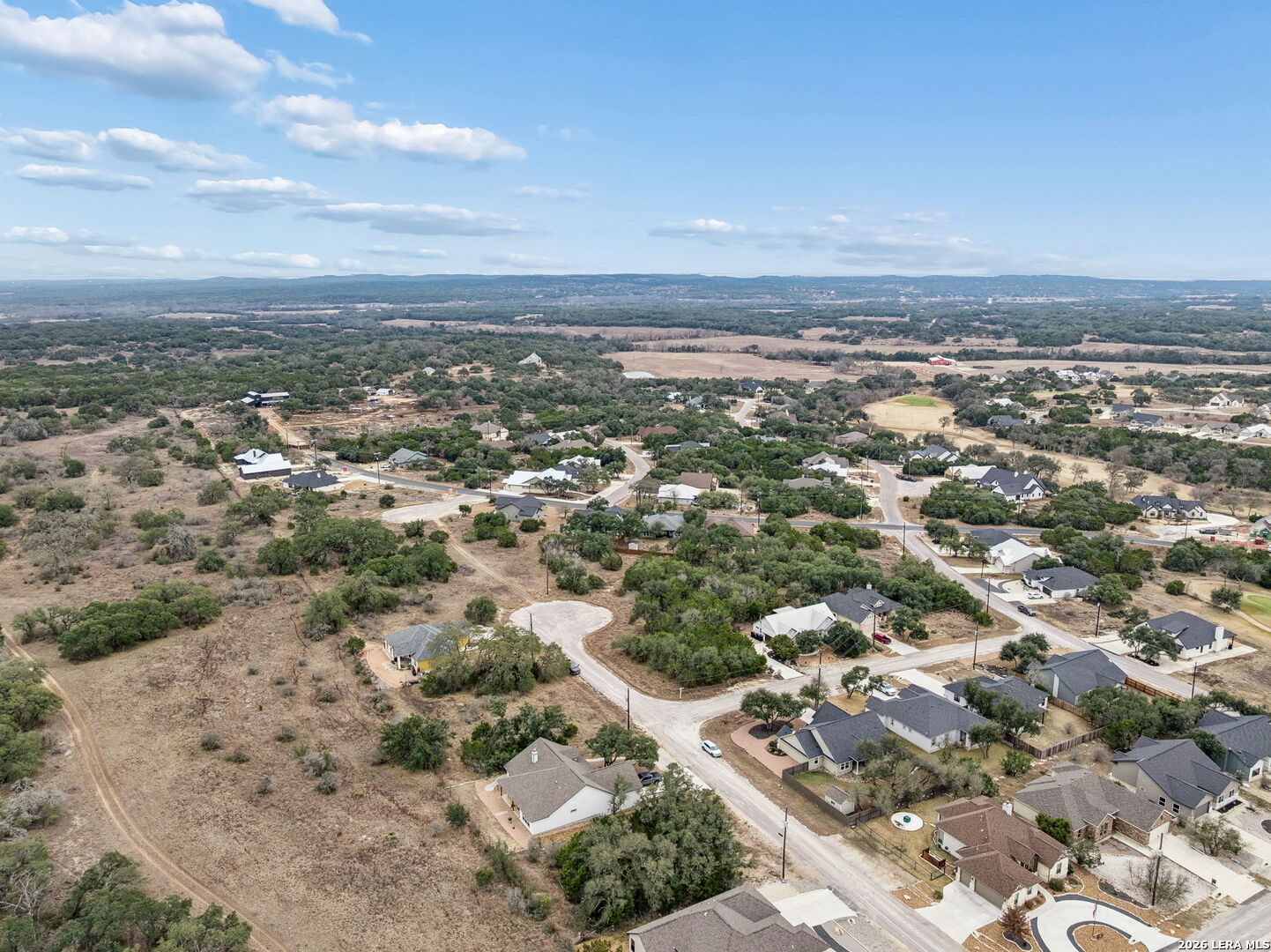 Aerial view of a residential neighborhood with winding roads, wooded lots, and open land.